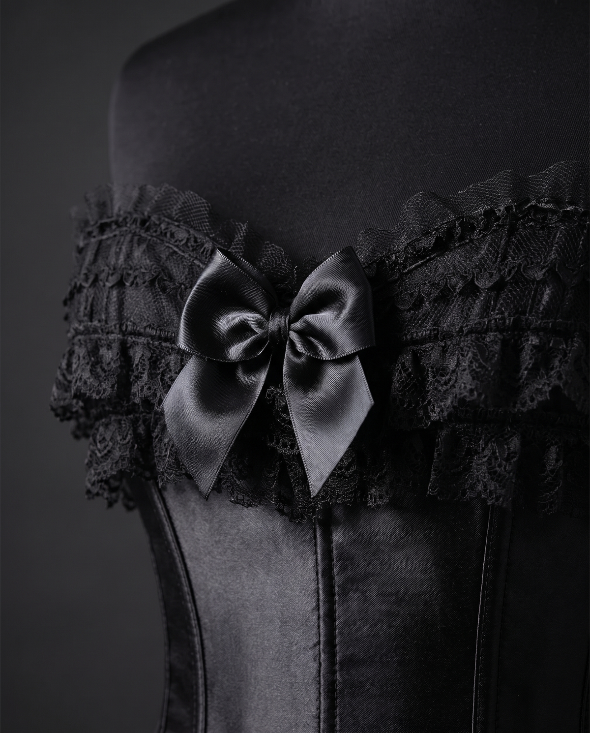 Close-up of the ruffled lace neckline and satin bow on a black corset