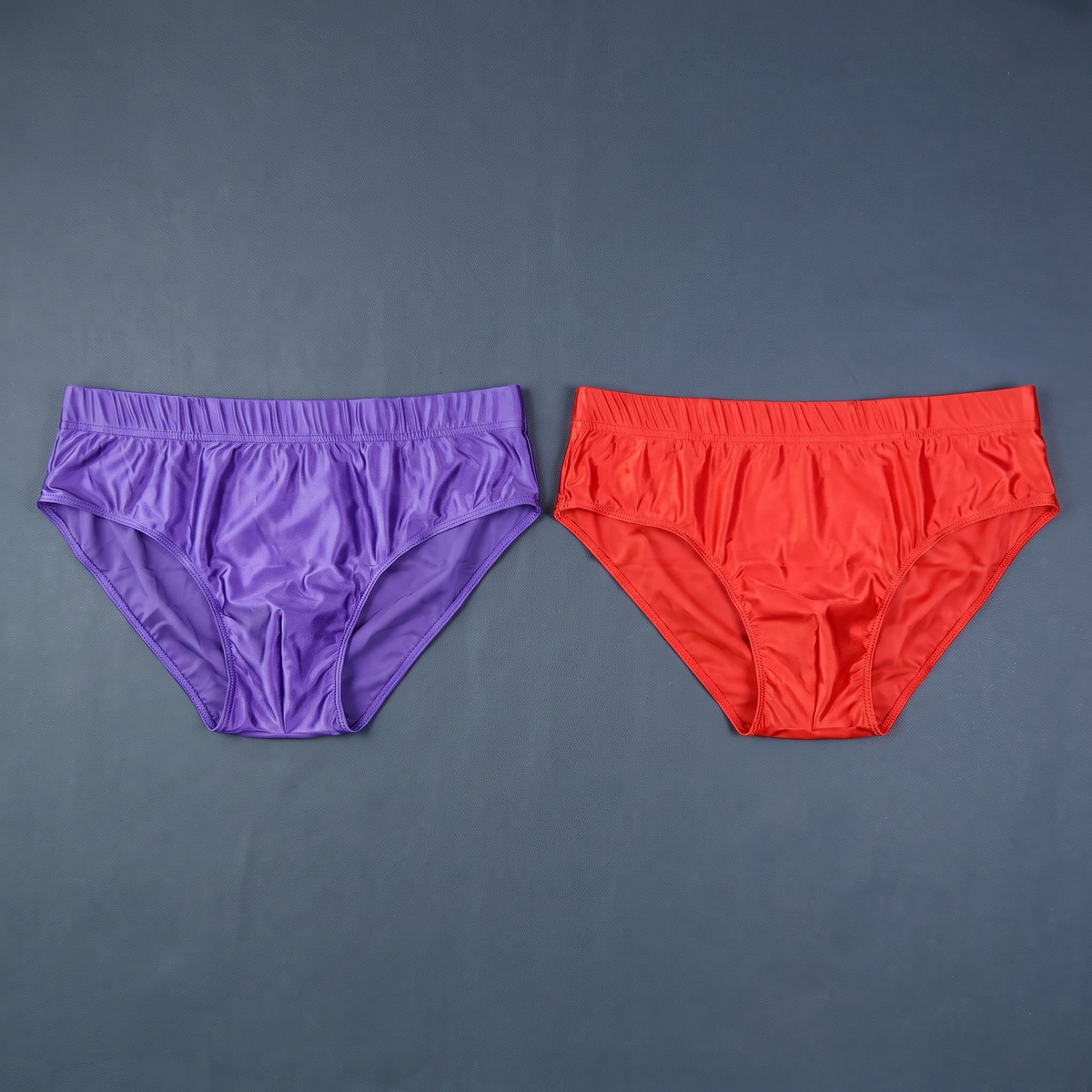 Purple and red men's satin-finish briefs laid flat on slate